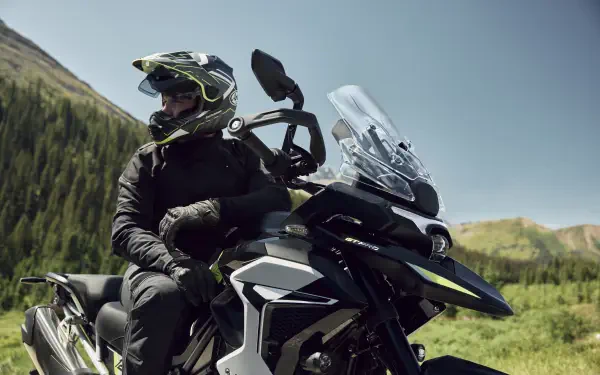 Helmeted motorcyclist riding a Triumph Tiger 1200 through a scenic mountain landscape, featured in 8K Ultra HD PC desktop wallpaper.