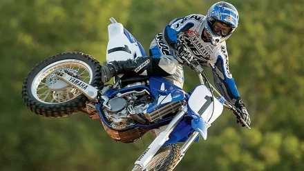 A Yamaha motocross rider in mid-air performing a stunt against a blurred green background, captured in high definition as a PC desktop wallpaper.