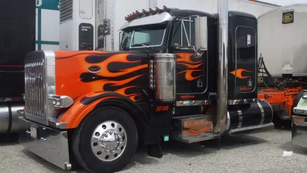 A striking HD desktop wallpaper featuring a black and orange truck adorned with fiery flame graphics, showcasing its powerful presence and sleek design.