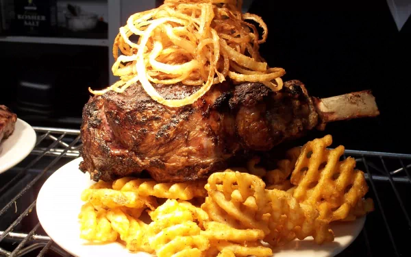 A delicious serving of meat topped with crispy onion rings, accompanied by golden waffle fries, presented as a vibrant HD desktop wallpaper and background.