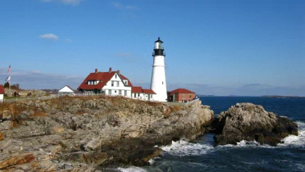 HD PC desktop wallpaper featuring a man-made lighthouse on the rocky coast of Maine under a clear blue sky with ocean waves crashing nearby.