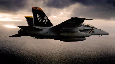 A Boeing F/A-18E/F Super Hornet flies over a dramatic ocean backdrop, showcasing its military prowess against a moody sky. HD wallpaper featuring a striking aircraft.