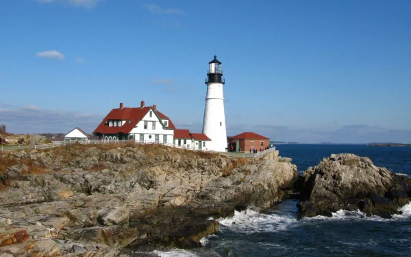 HD PC desktop wallpaper featuring a man-made lighthouse on the rocky coast of Maine under a clear blue sky with ocean waves crashing nearby.