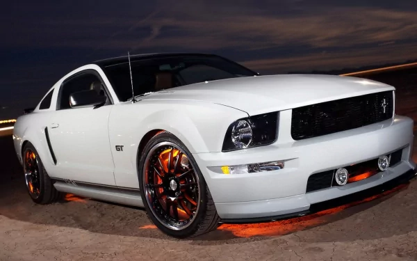HD PC desktop wallpaper of a white Ford Mustang GT with orange underglow and black rims, parked under a dramatic dusk sky.