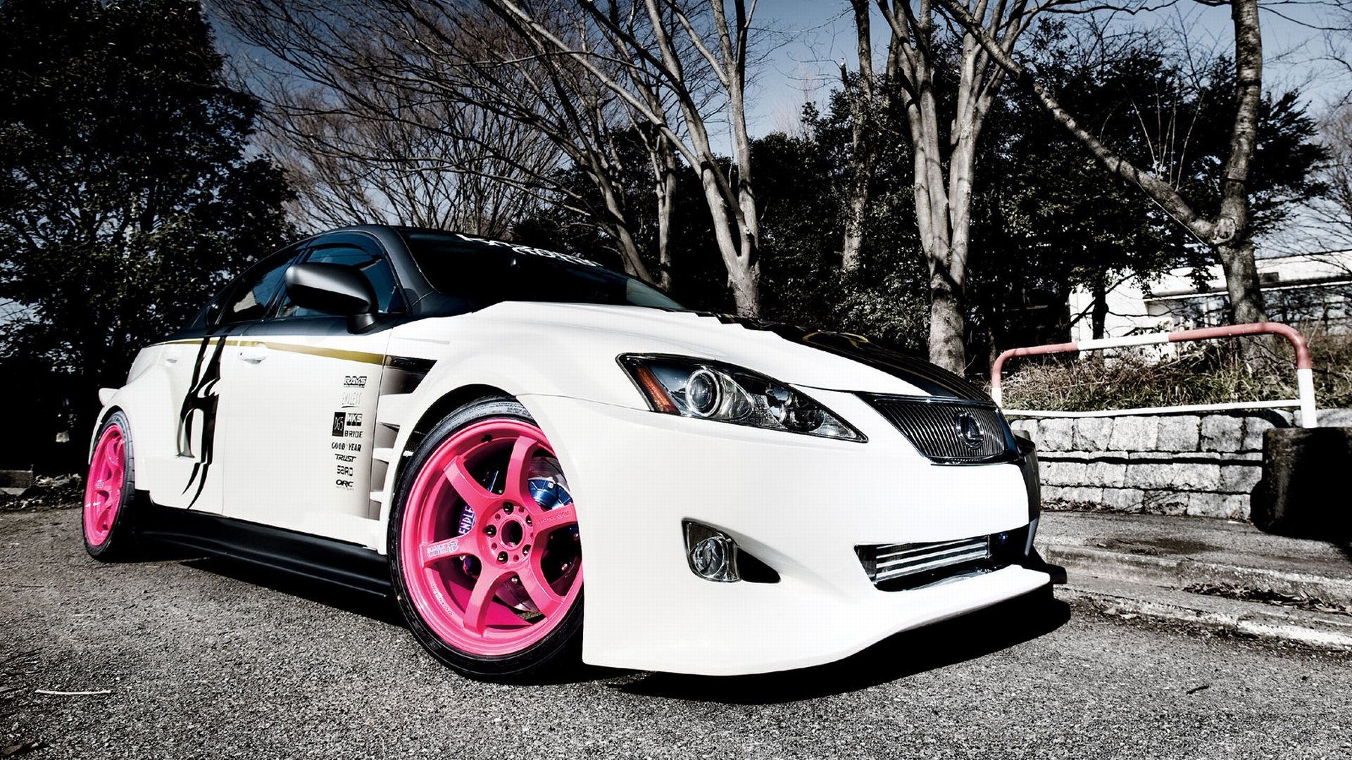 HD PC desktop wallpaper of a modified white Lexus vehicle — low, aggressive sports coupe with bright pink wheels parked by trees and a stone wall.