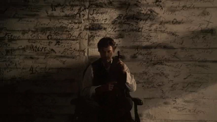 A dramatic still from Sherlock Holmes: A Game of Shadows features Sherlock sitting in a dimly lit room, holding a violin, with mysterious writings on the walls surrounding him.