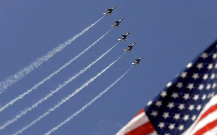 HD PC desktop wallpaper showing military jets in tight formation at an air show, trailing white smoke across a clear blue sky with a waving American flag in the corner.