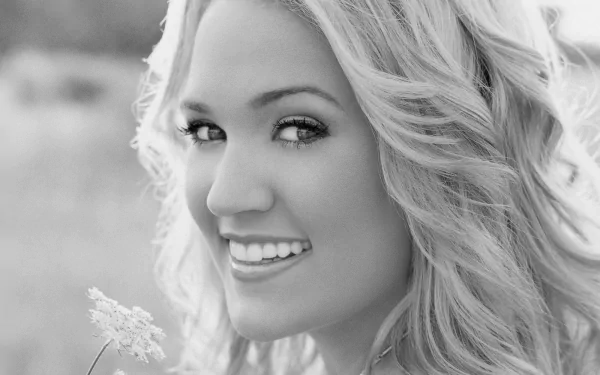 Black and white HD desktop wallpaper featuring a close-up portrait of Carrie Underwood smiling outdoors, highlighting her blonde hair and radiant expression.