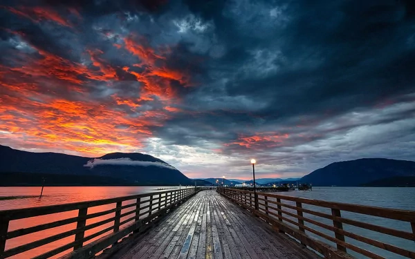 A captivating sunset over a wharf, with vibrant red and orange skies reflecting on the ocean. This striking HD wallpaper captures nature's beauty at dusk.