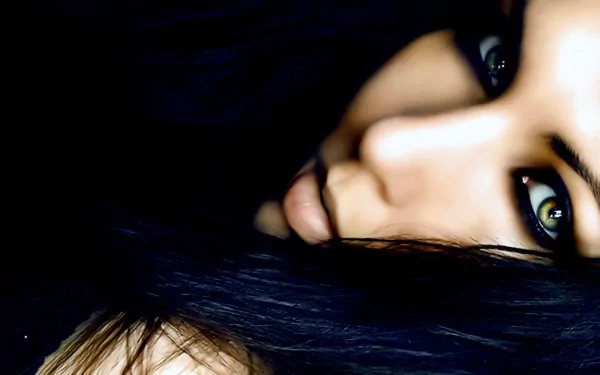 HD image of a woman's face with striking green eyes, dark hair, and dramatic lighting, suitable as a desktop wallpaper and background.