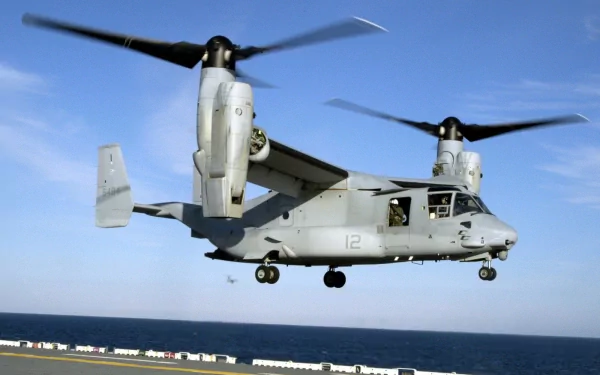HD PC desktop wallpaper showing a military Bell Boeing V-22 Osprey tiltrotor aircraft in gray hovering over the sea beneath a clear blue sky.
