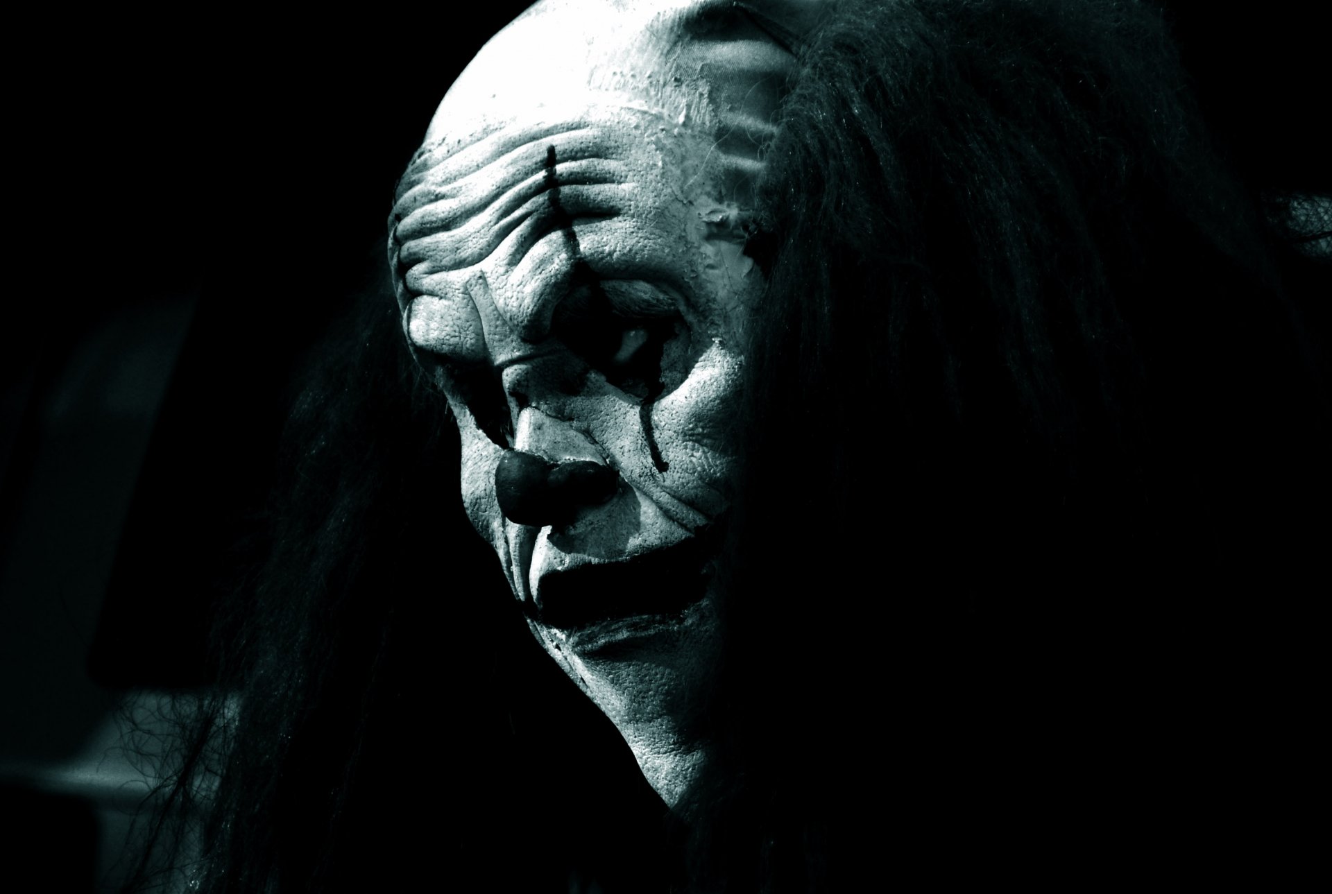 A dark, eerie clown mask with an unsettling expression, shrouded in shadows. This HD wallpaper adds a chilling atmosphere to any desktop background.