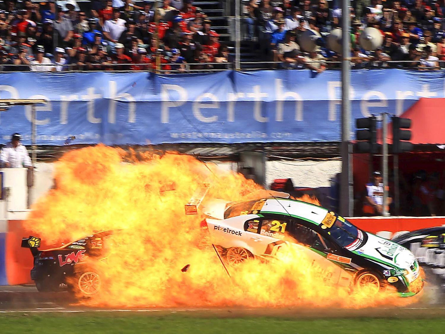 HD PC desktop wallpaper showing a sports car racing through flames at a packed track; vehicle skids amid a dramatic fiery crash.