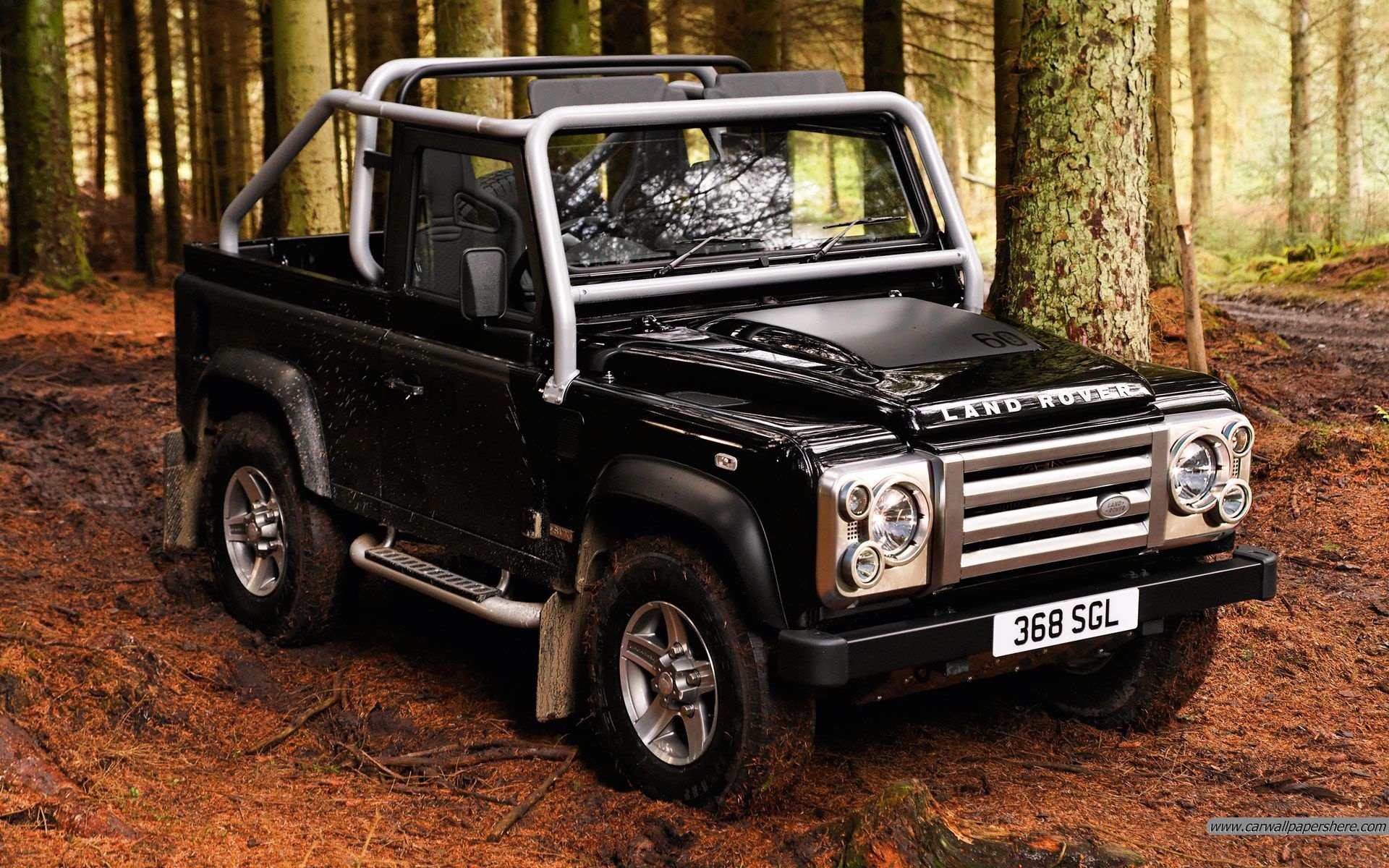 Black Land Rover parked on a forest floor, captured in an HD PC desktop wallpaper showcasing the rugged vehicle amid tall trees.
