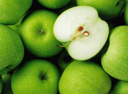 A vibrant HD desktop wallpaper featuring fresh green apples, including one sliced in half to reveal its juicy interior, providing a fresh and appetizing look.