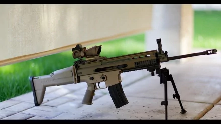 HD desktop wallpaper showcasing a man-made FN SCAR assault rifle resting on a bipod with a blurred outdoor background.
