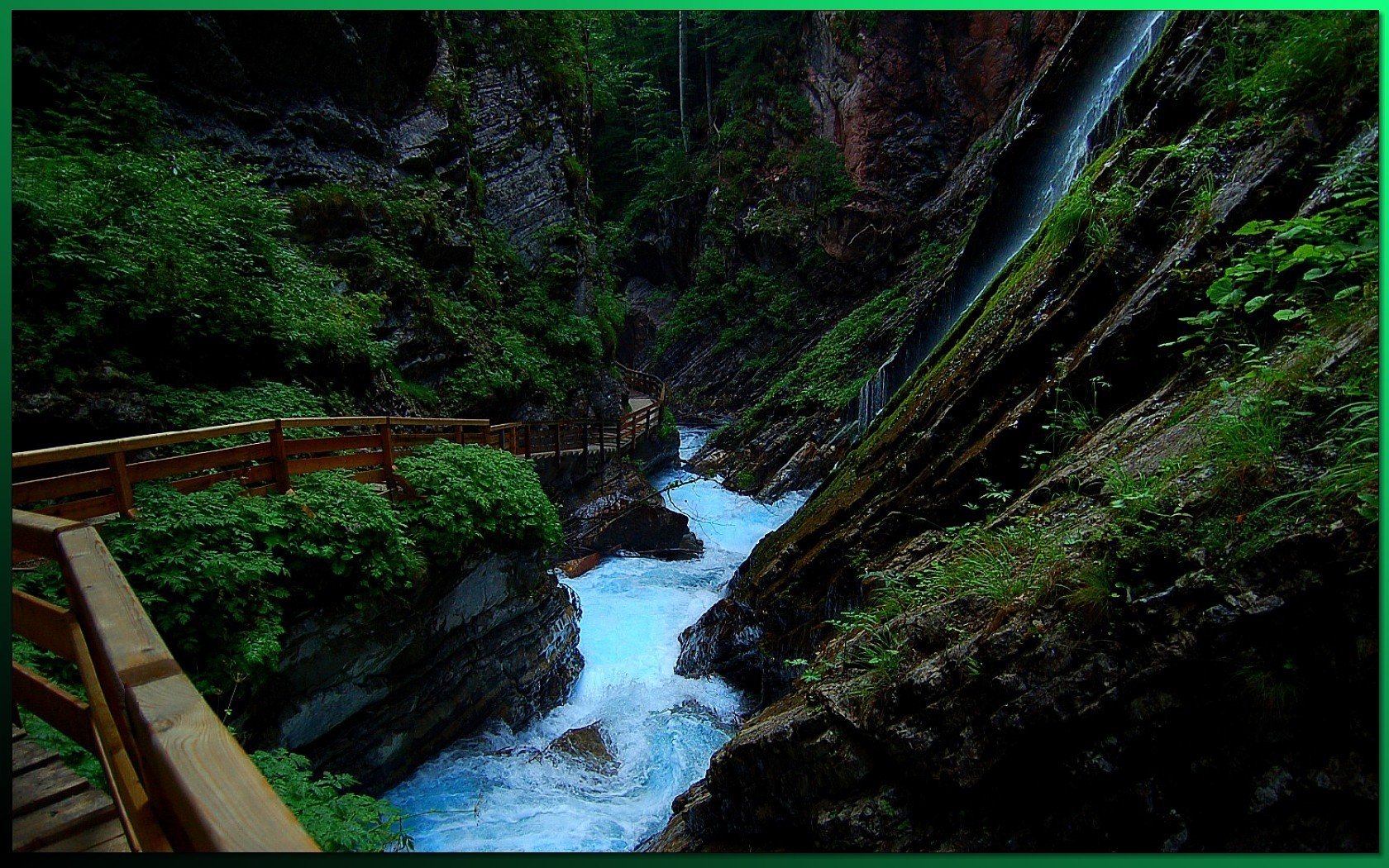 HD PC desktop wallpaper of a lush forest gorge: a wooden walkway beside a rushing mountain stream and narrow waterfall cutting through mossy rocks.