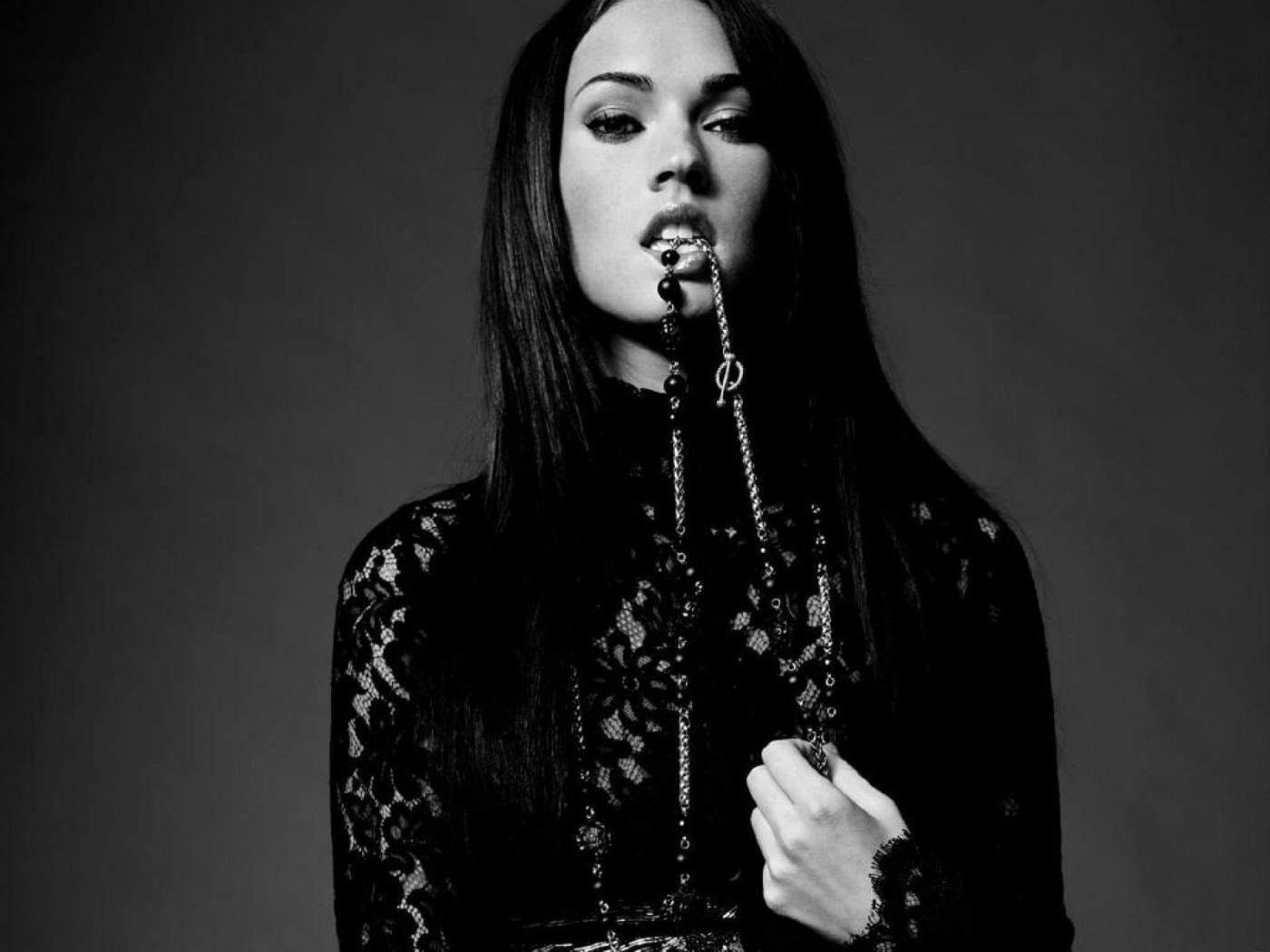 Black-and-white HD desktop wallpaper of celebrity Megan Fox wearing lace, with a chain accessory held in her mouth against a dark background.