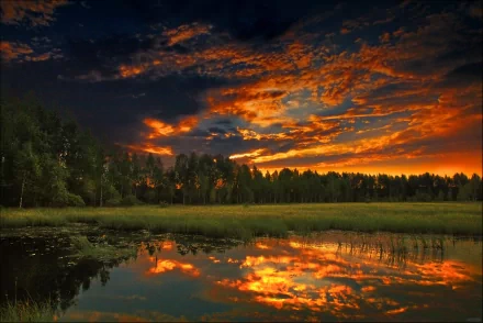 HD desktop wallpaper featuring a stunning nature scene with a vibrant sunset reflecting on a calm lake surrounded by lush green forest and grasslands.