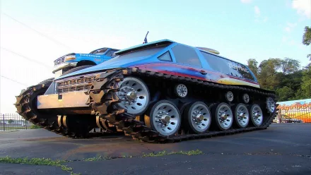 HD desktop wallpaper featuring a colorful monster truck with large wheels and tank-like tracks, set against an outdoor background.
