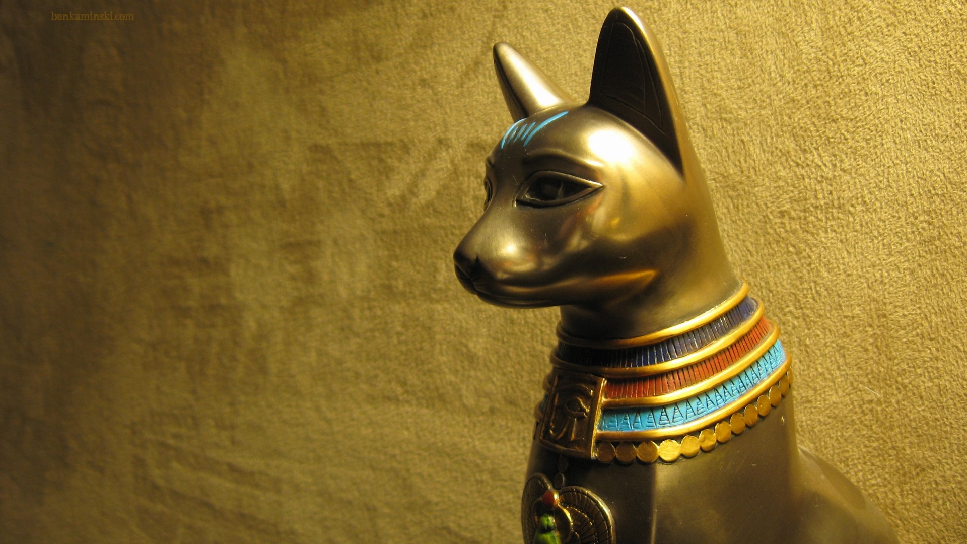 4K Ultra HD PC desktop wallpaper of an Egyptian golden man-made statue: a gilded cat figure with an ornate blue-and-red collar against a textured gold background.