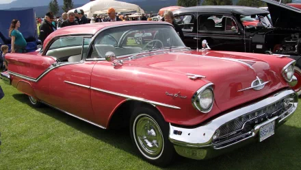 HD desktop wallpaper featuring a classic red Oldsmobile parked on grass at a car show, surrounded by other vintage vehicles and attendees.