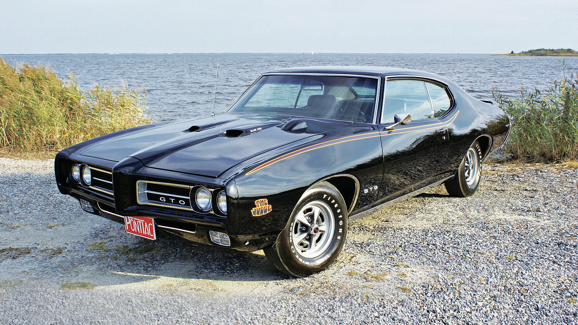 Black Pontiac GTO muscle car on a scenic road, surrounded by nature