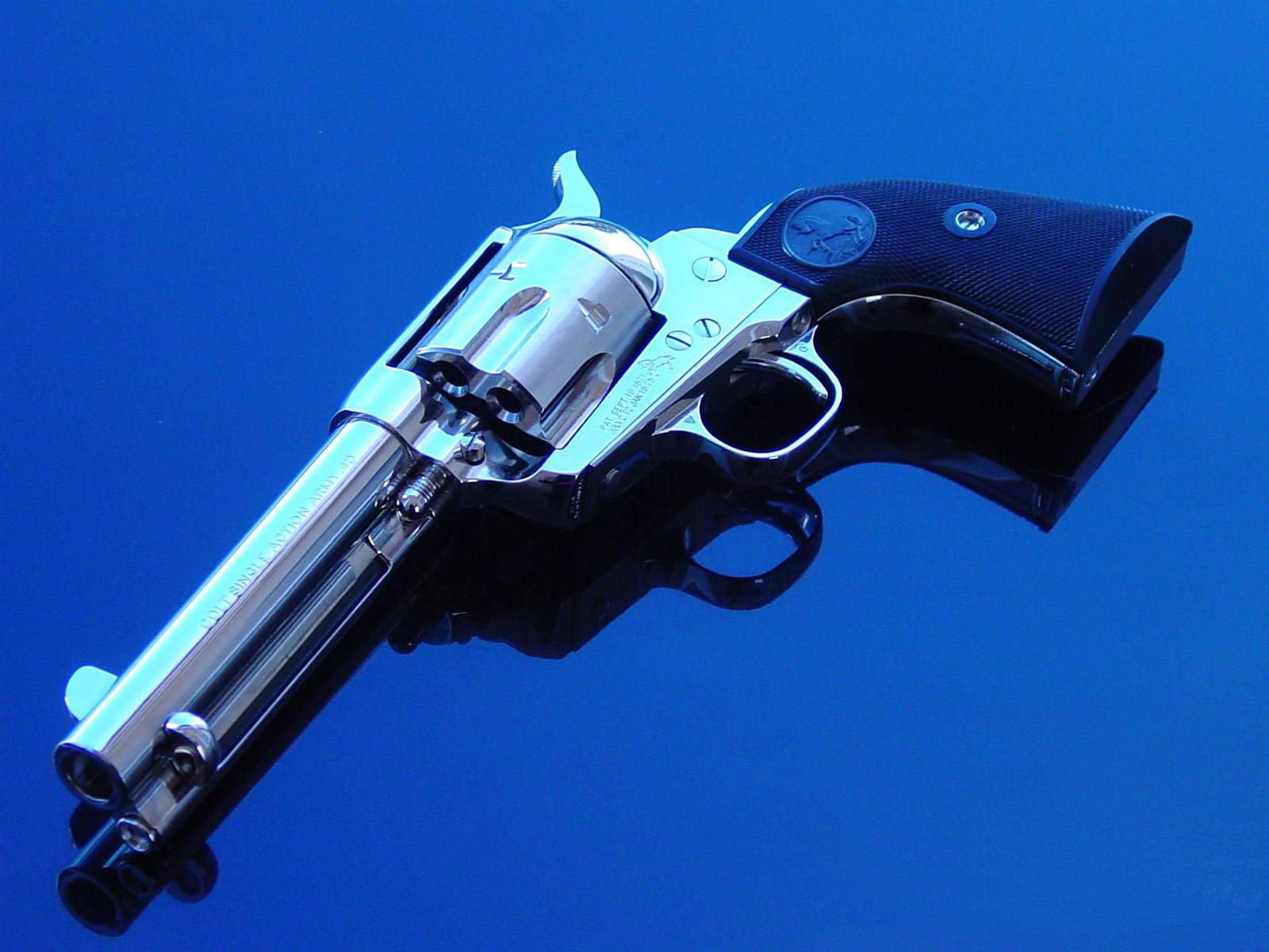 HD desktop wallpaper of a shiny Colt revolver with black grips against a solid blue background, highlighting the man-made firearm's metal details.