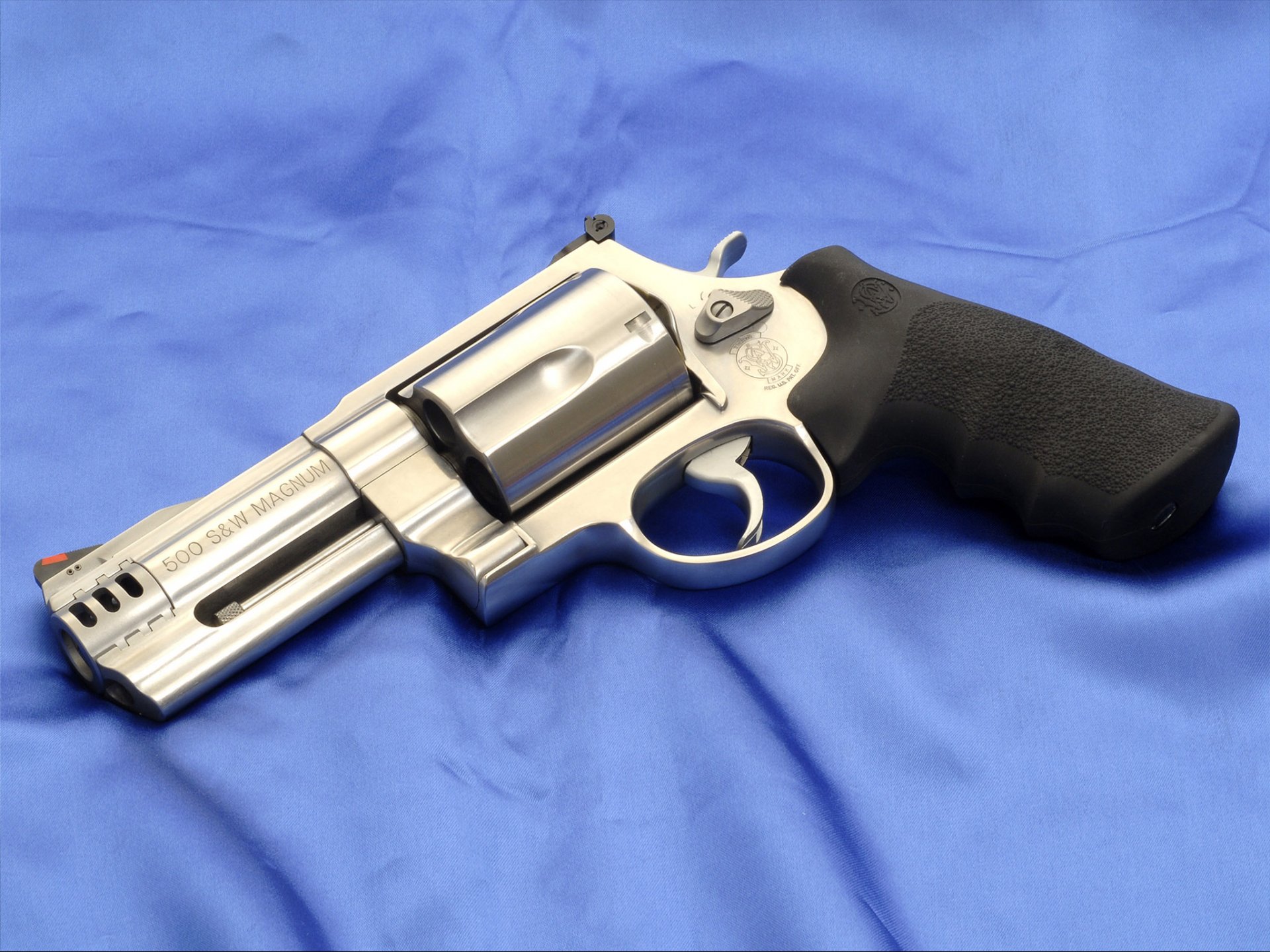 HD desktop wallpaper featuring a man-made Smith & Wesson Model 500 revolver with a stainless steel finish and black grip on a blue fabric background.