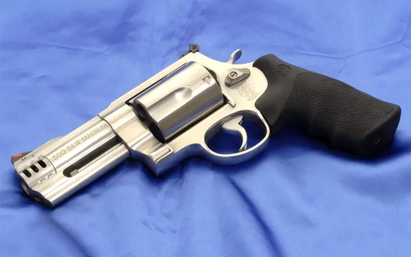 HD desktop wallpaper featuring a man-made Smith & Wesson Model 500 revolver with a stainless steel finish and black grip on a blue fabric background.