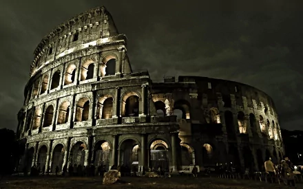 HD desktop wallpaper of the illuminated man-made Colosseum at night, showcasing its ancient architectural arches against a dark sky.