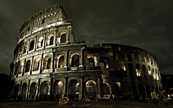HD desktop wallpaper of the illuminated man-made Colosseum at night, showcasing its ancient architectural arches against a dark sky.
