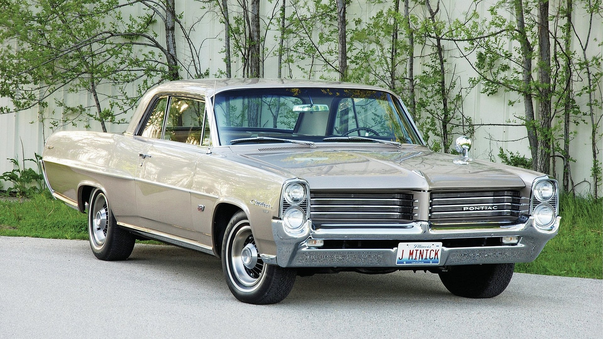 HD PC desktop wallpaper showing a classic Pontiac vehicle: tan 1960s coupe in a front three-quarter view parked by trees.