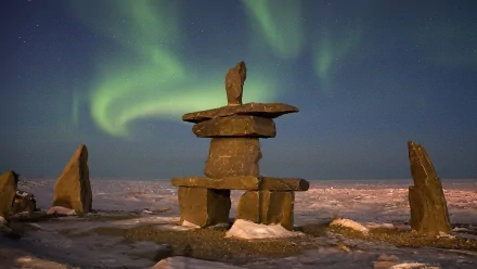 HD desktop wallpaper featuring a serene natural scene with a stone inukshuk under vibrant green aurora borealis lights in the night sky.