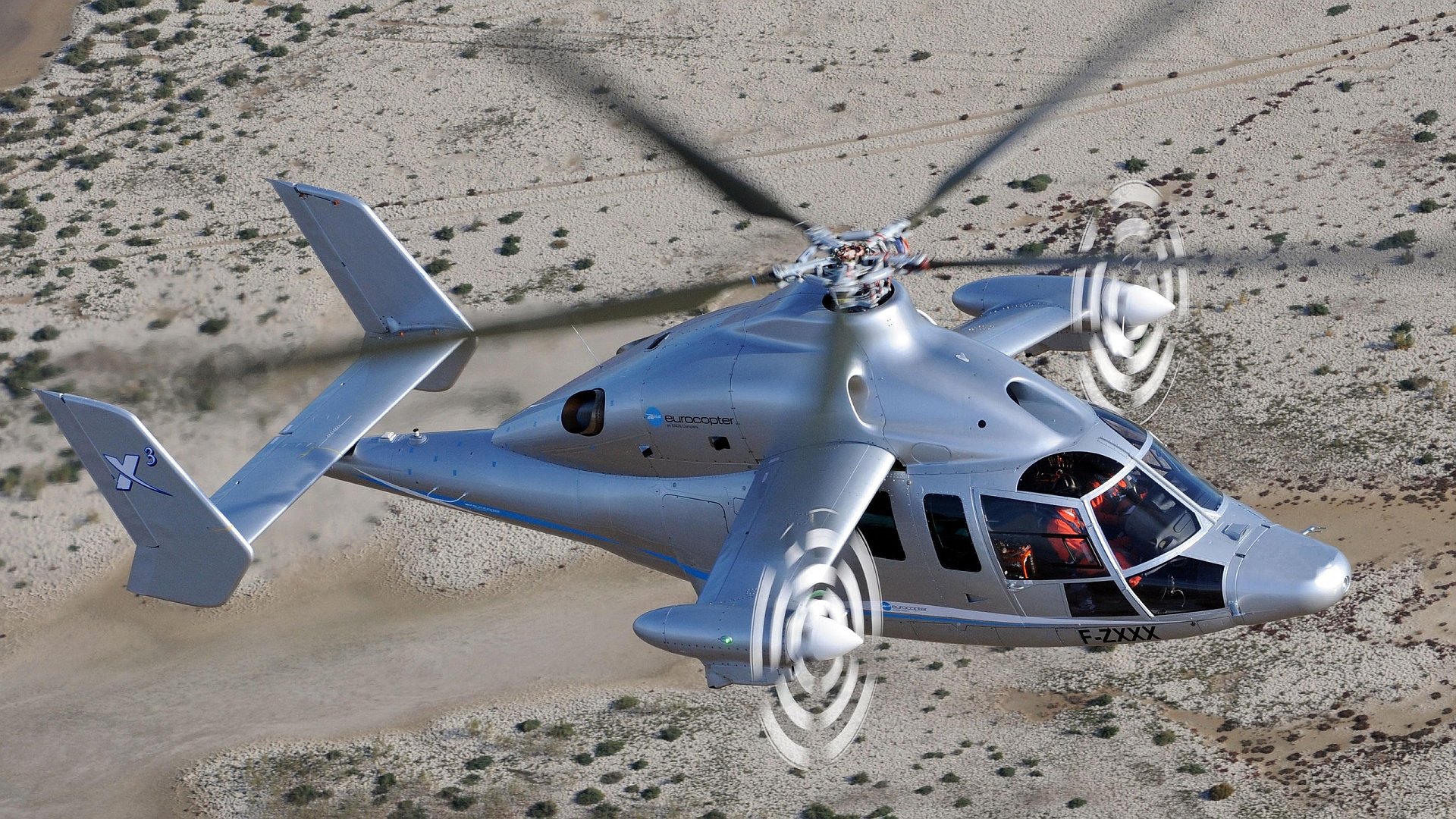 HD desktop wallpaper featuring a Eurocopter X3 helicopter in flight over a desert landscape.
