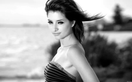 Black-and-white HD PC desktop wallpaper: a celebrity portrait of a smiling woman by the water, windblown hair and a strapless striped top, soft-focus shoreline background.