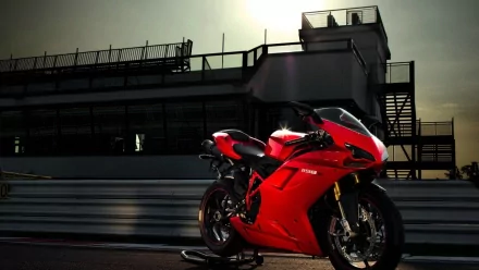HD PC desktop wallpaper showing a red Ducati sport motorcycle vehicle parked on a racetrack at dusk, dramatic lighting and a modern grandstand in the background.