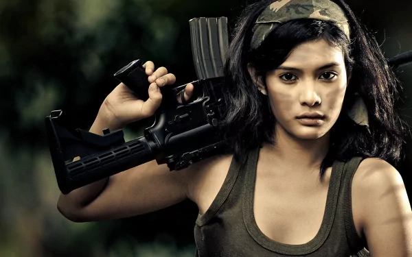 A confident woman holding a gun, wearing a tank top and headband, set against a blurred outdoor background. This HD wallpaper captures strength and determination.