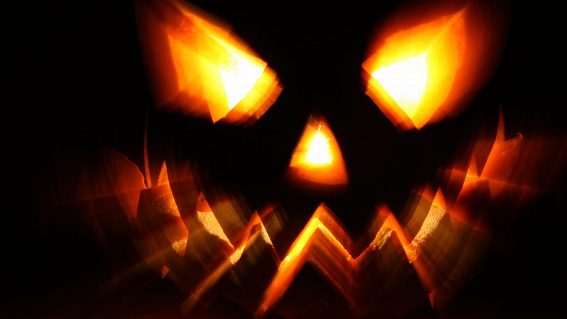 HD PC desktop wallpaper featuring a glowing, menacing jack-o'-lantern face with fiery eyes and mouth, capturing the Halloween holiday spirit.