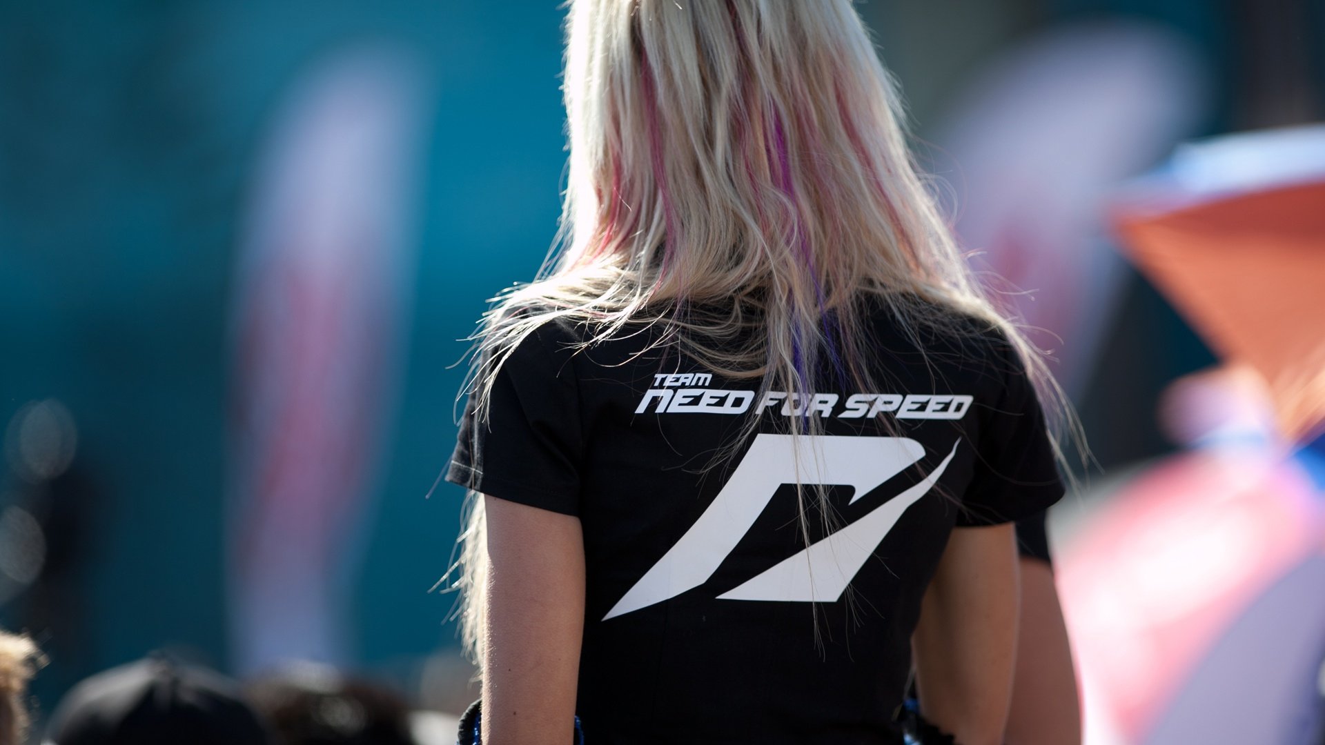 HD PC desktop wallpaper featuring a person wearing a black Need For Speed team T-shirt, set against a blurred outdoor background.