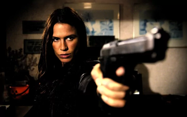 HD PC desktop wallpaper featuring Rhona Mitra from the movie Skinwalkers, aiming a handgun with an intense expression in a dimly lit setting.