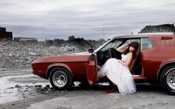 A woman in a flowing white dress poses next to a classic red car in a rugged landscape, creating a striking contrast in this HD desktop wallpaper.