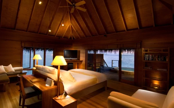 4K Ultra HD wallpaper of a cozy, man-made wooden room with a high vaulted ceiling, warm lighting, and large windows overlooking a serene waterfront.