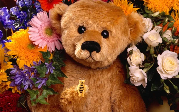 A high-definition desktop wallpaper featuring a stuffed teddy bear surrounded by an array of vibrant flowers, including roses, daisies, and lilies.
