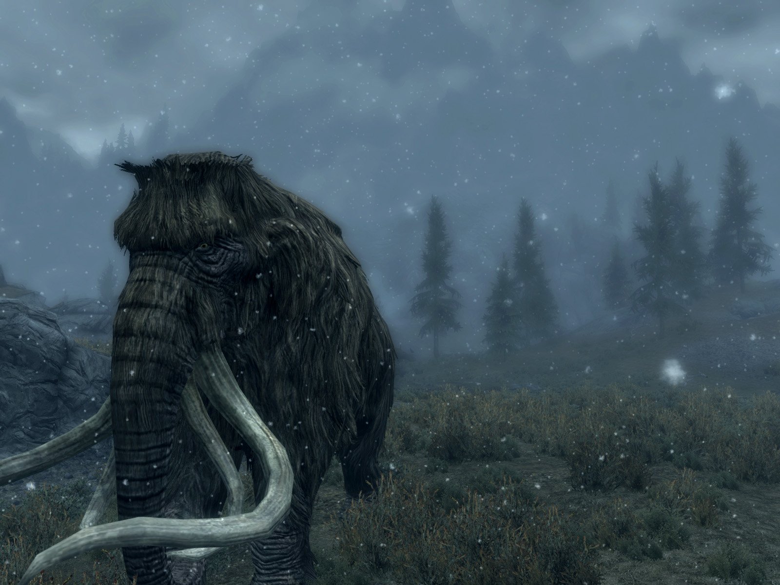 A mammoth stands in a snowy landscape from The Elder Scrolls V: Skyrim, surrounded by trees, creating a captivating scene for an HD PC desktop wallpaper.