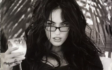 Megan Fox poses confidently with a glass in hand against a backdrop of palm leaves, captured in a striking black-and-white HD desktop wallpaper.