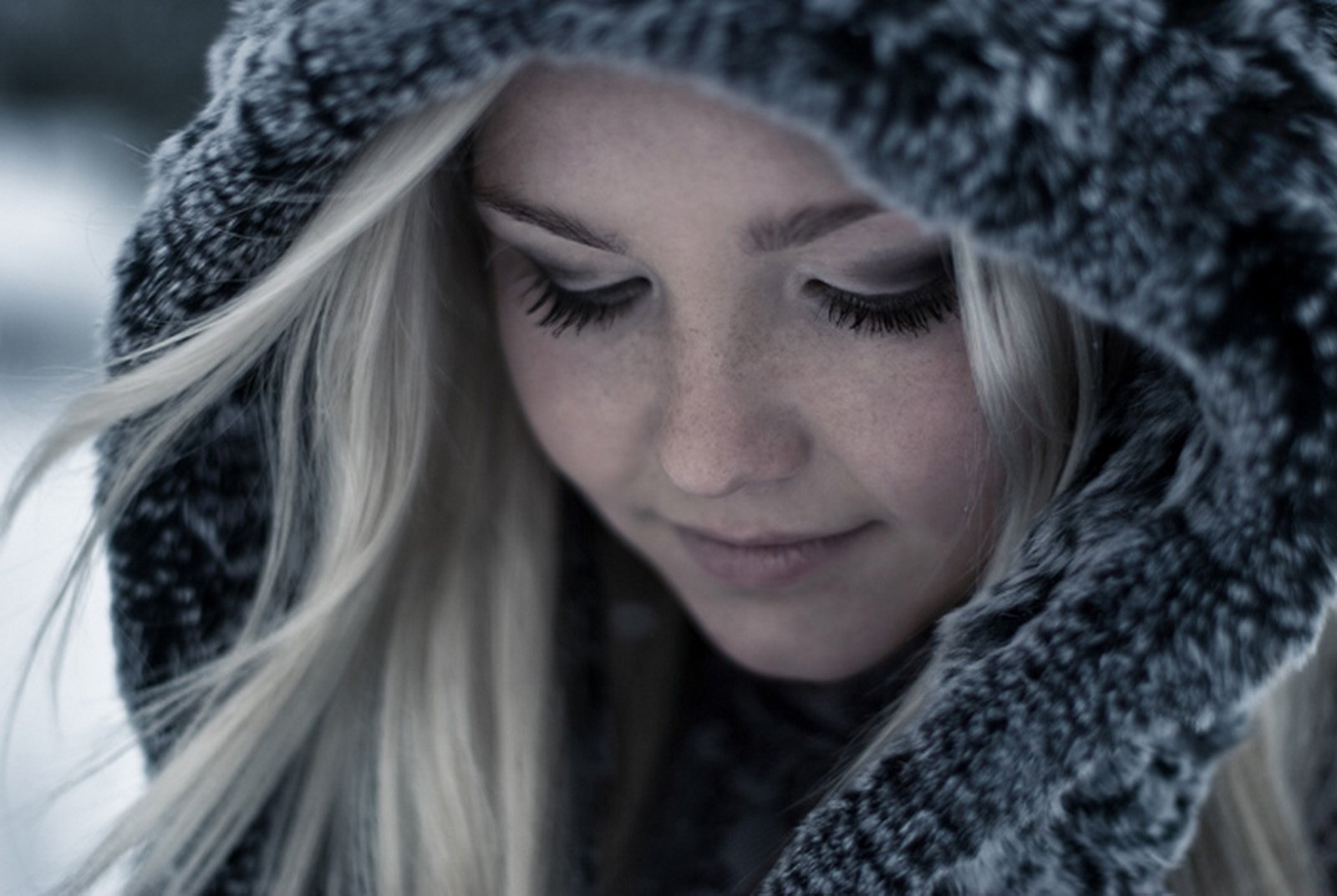 A serene, close-up HD desktop wallpaper of a woman model with closed eyes, wearing a thick, textured hooded garment, standing in a cold, wintry setting.