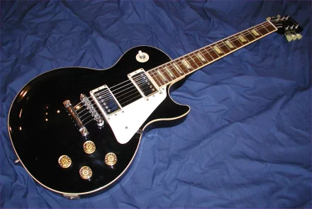 An HD desktop wallpaper featuring a black electric guitar with a white pickguard, resting on a blue background.