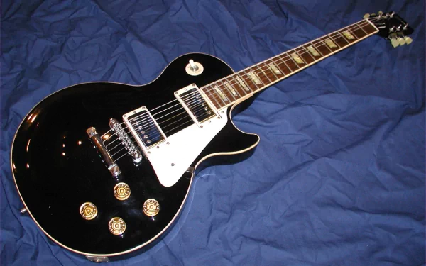 An HD desktop wallpaper featuring a black electric guitar with a white pickguard, resting on a blue background.