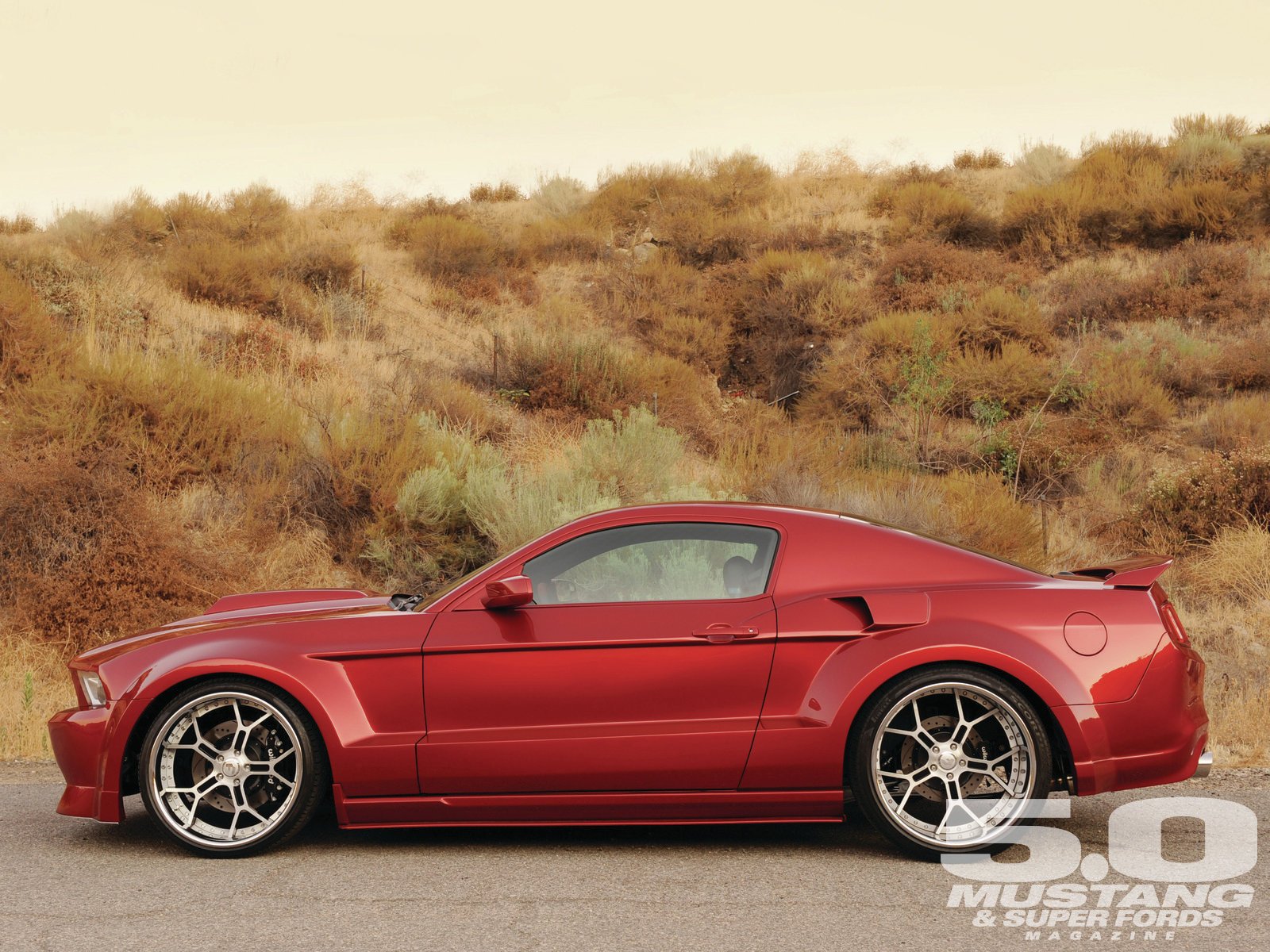 HD PC desktop wallpaper featuring a red Ford sports car parked in front of a dry, shrub-covered hillside.
